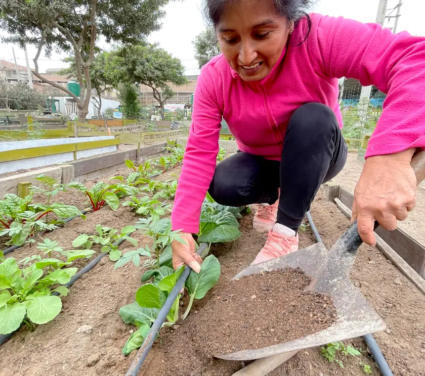 Mujer regando un huerto comunitario abonado con compost