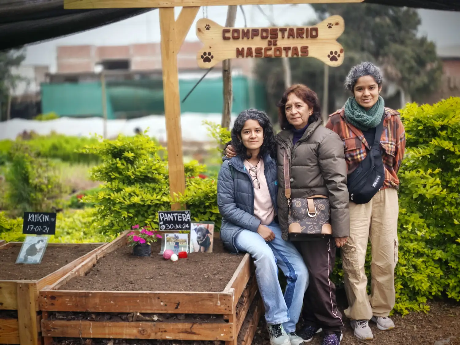 Familias sentadas junto a las cunas composteras del camposanto de mascotas, bajo el cartel Compostario de Mascotas