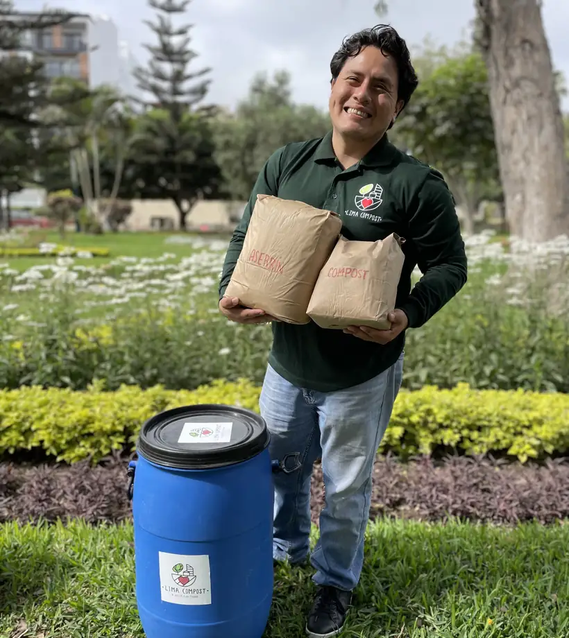 Bidón de recojo de Lima Compost junto a bolsas de compost en un jardín